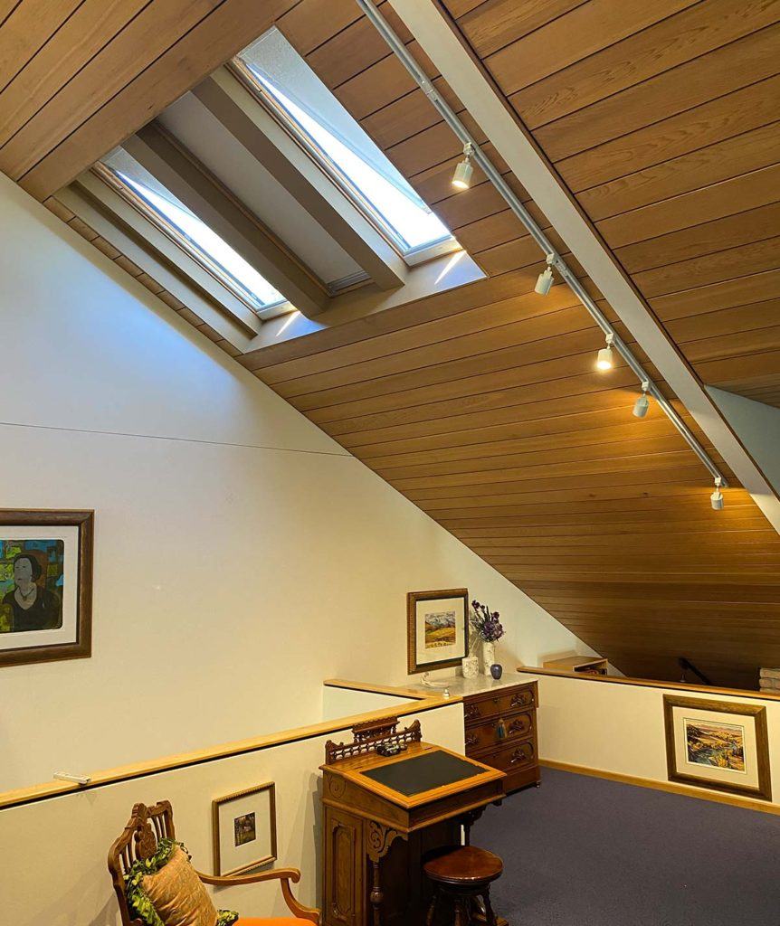 a loft office with a wood slanted ceiling and track lighting