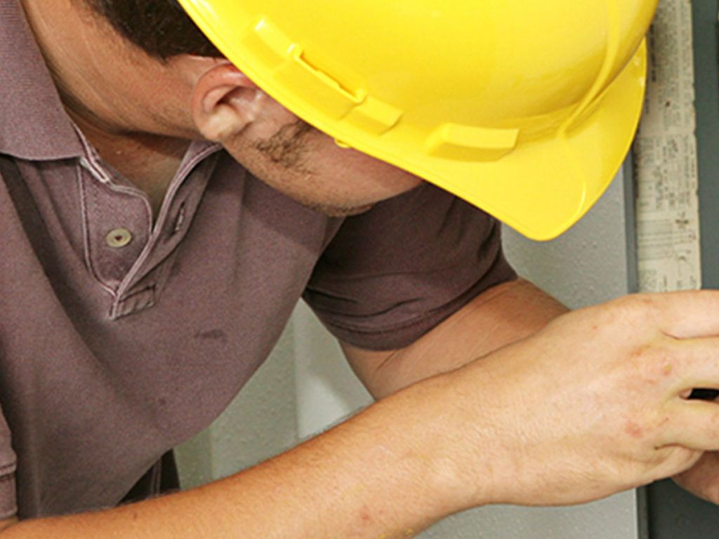 a close up photo of a man in a yellow hard hat working on an electric panel