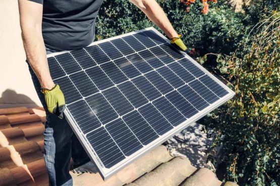 a man holding a solar panel on top of a residential roof