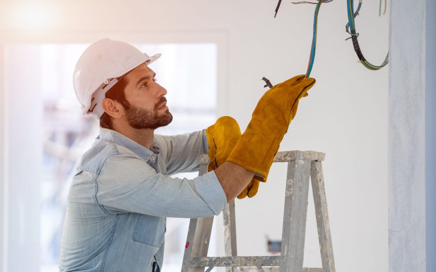 man in white hard hat, safety gloves and a blue work shirt working on electrical wiring